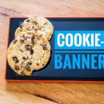 Tablet zeigt Cookie-Banner-Hinweis. Auf dem Display liegen zwei echte Kekse.