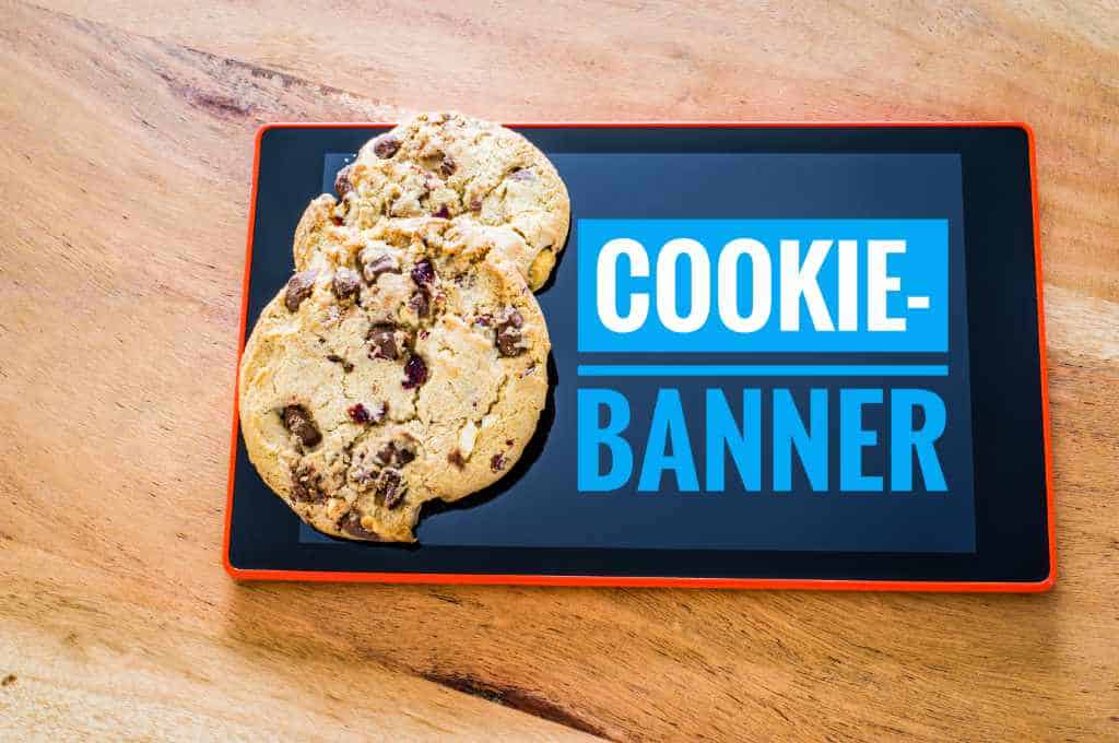 Tablet zeigt Cookie-Banner-Hinweis. Auf dem Display liegen zwei echte Kekse.